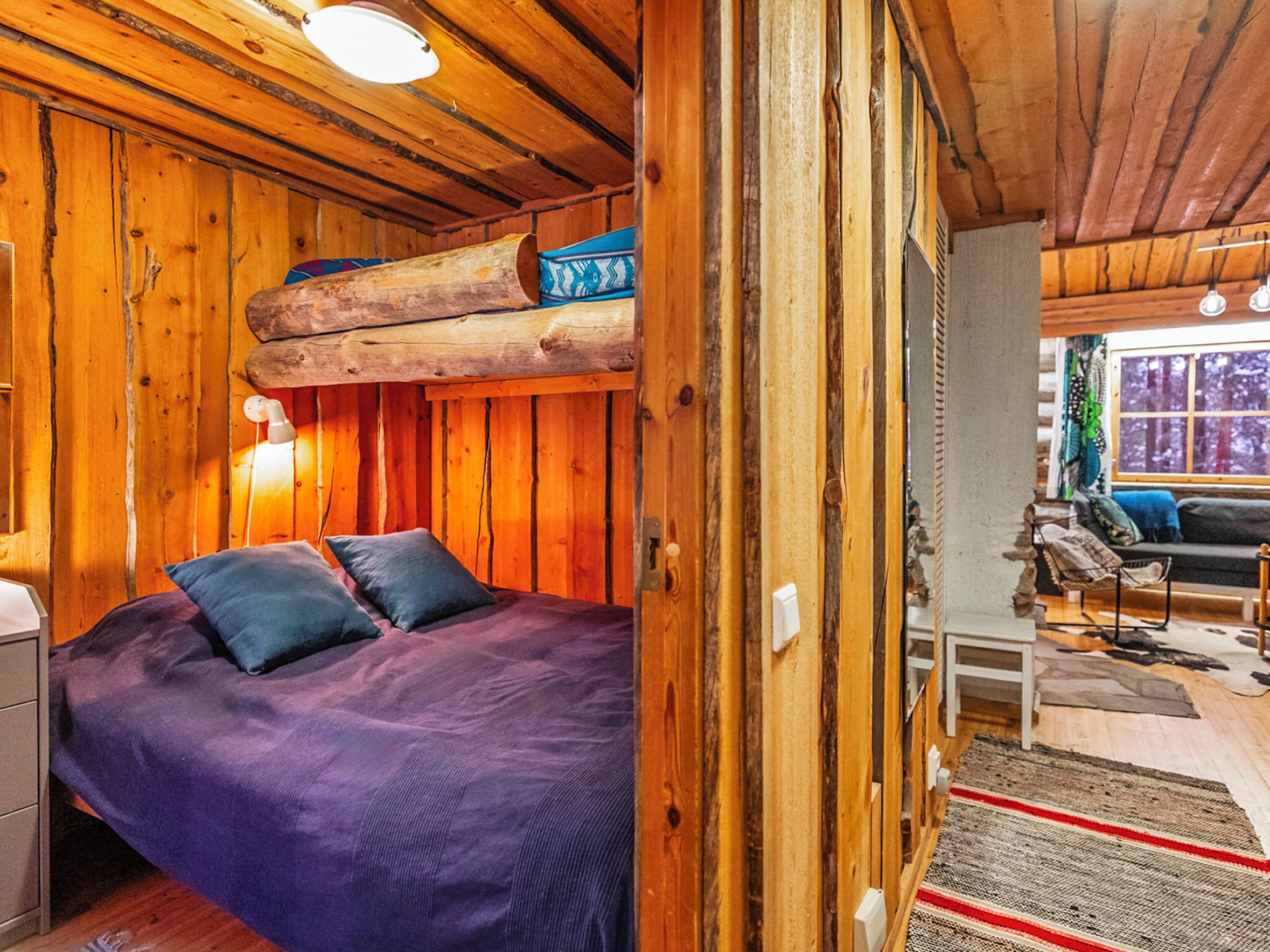 A cozy cabin-style room with a bed, wooden walls, a loft bed, and a window with a view.