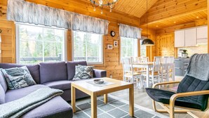 Ein gemütliches Blockhaus-Interieur mit Sofa, Esstisch, Stühlen, Holzwänden und großen Fenstern.