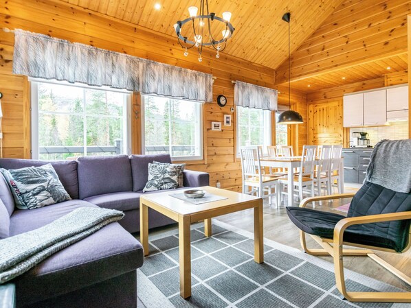 A cozy cabin interior with a sofa, dining table, chairs, and a kitchen area.