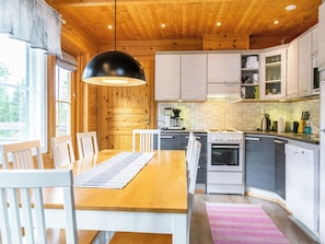 A modern kitchen with wooden cabinets, a dining table with chairs, and a hanging light fixture. - Tunturikettu by Interhome (Pelkosenniemi)