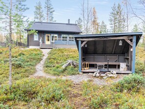 A cabin with a deck and a covered outdoor seating area, surrounded by a forested landscape. - Tunturikettu by Interhome (Pelkosenniemi)