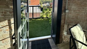 Ein Balkon mit Glastür, der zu einer Rasenfläche und einer Ziegelwand führt.
