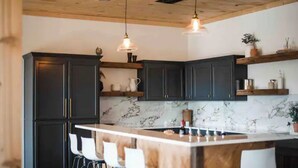 Eine moderne Küche mit dunklen Schränken, einer Marmor-Spritzschutzwand und einer Holzinsel mit Barhocker.