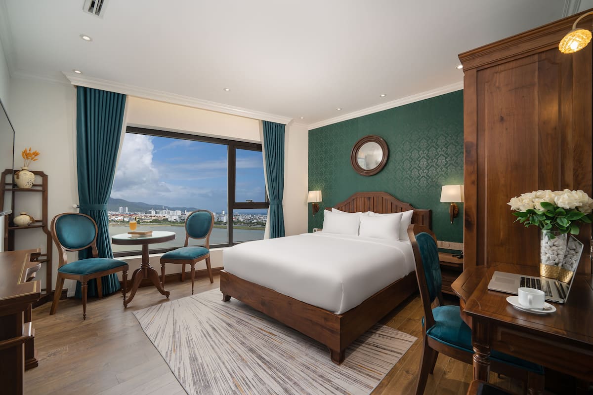 Une chambre d’hôtel avec un grand lit, deux fauteuils, un bureau et une vue sur la ville.