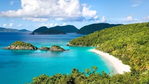 Un paisaje costero con una playa, aguas turquesas cristalinas y abundante vegetación.