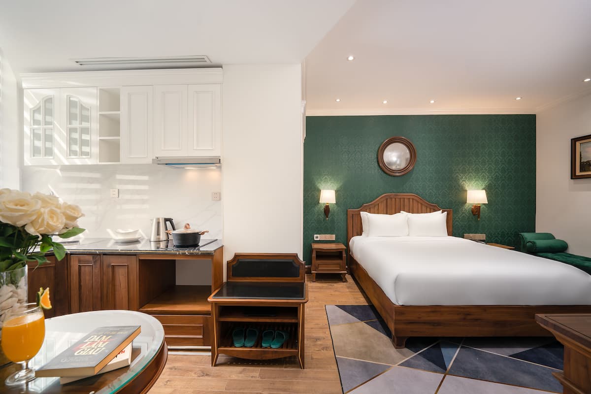 Une chambre d’hôtel comprenant un lit, des tables de chevet, un bureau avec une chaise, un petit coin cuisine et une salle de bain.