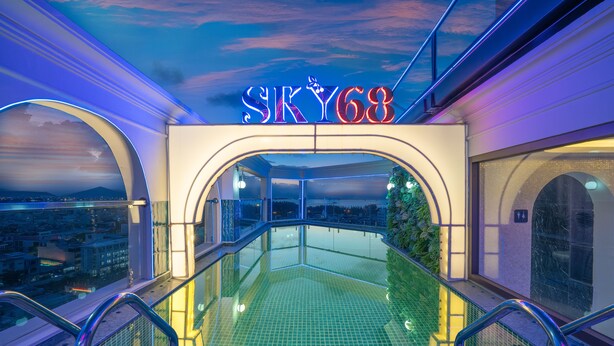 Una piscina infinita en la azotea con vistas a la ciudad, un letrero de neón que dice "SKY68" y una barandilla de cristal.