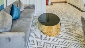 Un moderno vestíbulo de hotel con piso estampado, un sofá con cojines azules, una mesa de centro redonda y un techo decorativo.