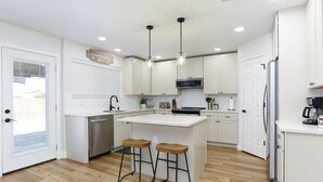 A modern kitchen with white cabinets, a central island with stools, stainless steel appliances, and pendant lighting. - Champions Getaway (San Antonio)