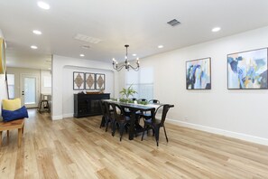 Uma sala de jantar espaçosa com piso de madeira, uma mesa central com cadeiras e um lustre.