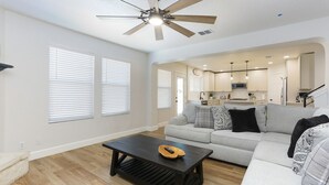 A spacious living room with a modern ceiling fan, a grey sofa, and a wooden coffee table. - Champions Getaway (San Antonio)