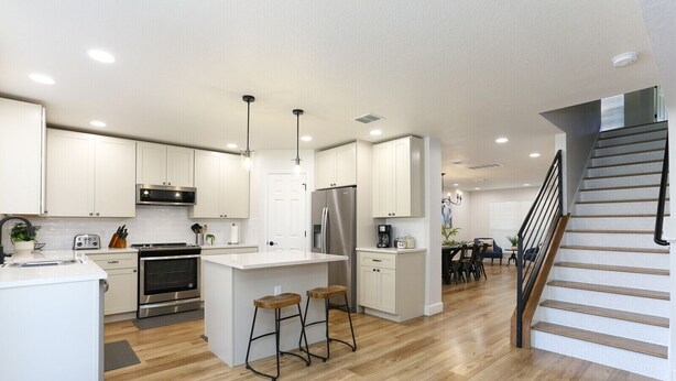 A modern kitchen with white cabinets, stainless steel appliances, and a central island with stools. - Champions Getaway (San Antonio)