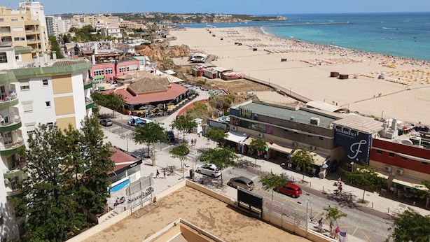 A coastal cityscape with a beach, buildings, and a restaurant named "BRITISH ROVER". - Varandas da Rocha 7 (Portimão)