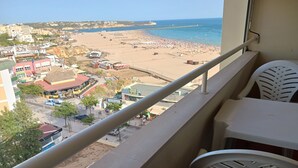 A balcony with a view of a beach, a parking area, and buildings in the background. - Varandas da Rocha 7 (Portimão)