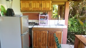 A compact kitchen with wooden cabinets, a refrigerator, a sink, and a small dining area with chairs. - Berkey's Jungle Paradise (Roseau)