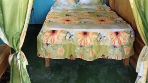 A single bed with a floral bedspread and green curtains. - Berkey's Jungle Paradise (Roseau)