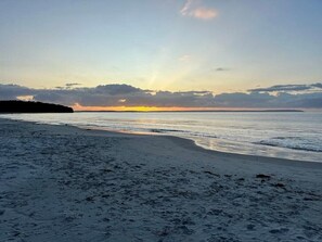 A beach with a sunset view, sandy shore, and calm sea. - Family friendly holiday home (Callala Beach)