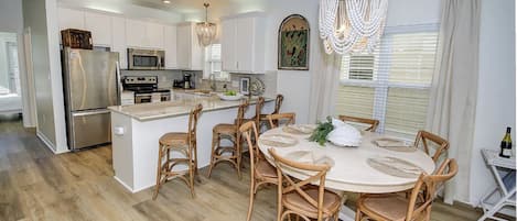 Una cocina moderna con armarios blancos, electrodomésticos de acero inoxidable, una isla central con asientos y una lámpara de araña.