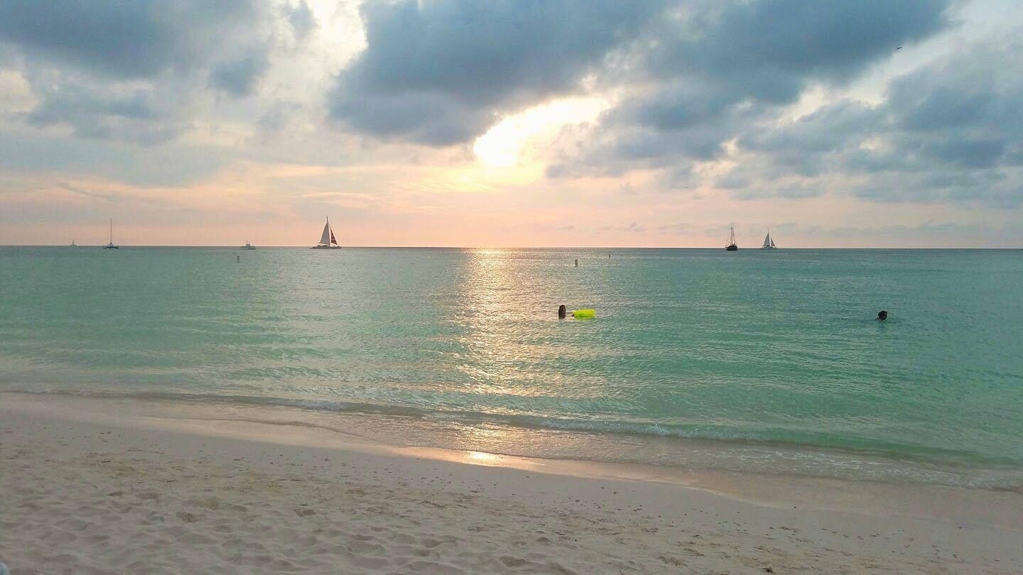 Una playa con aguas tranquilas y barcos a lo lejos.