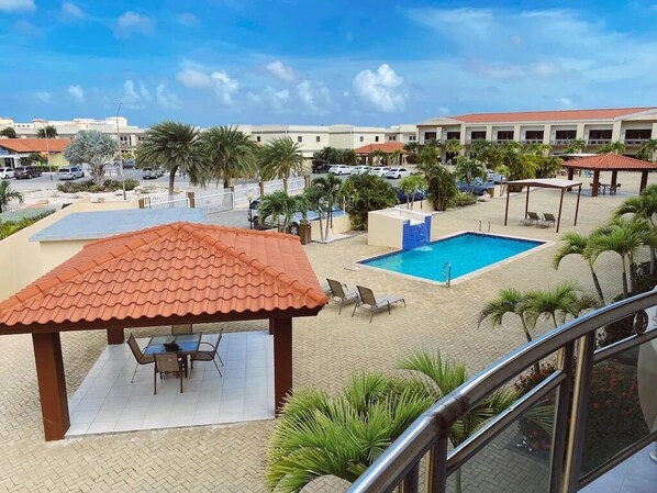 A hotel pool area with a covered seating area, lounge chairs, and a clear view of the surrounding buildings.