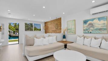 Un salon moderne avec vue sur la piscine, comprenant deux canapés, une table ronde et des œuvres d’art accrochées aux murs.