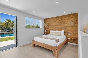 Une chambre avec un grand lit, un lambris en bois, une table de chevet, une lampe et une vue sur une piscine.