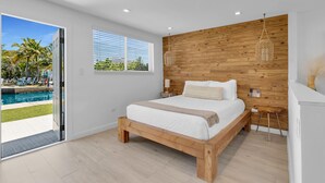 A bedroom with a wooden headboard, a large bed, a bedside table with a lamp, and a view of a swimming pool outside. - 3. Waterfront Key Largo Studio | Scuba & Dock (Key Largo)