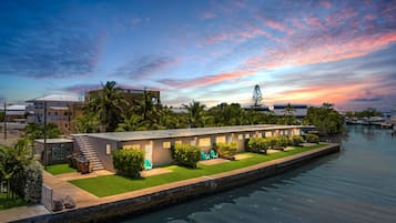 A waterfront hotel with a row of rooms, a grassy lawn, and a calm river.