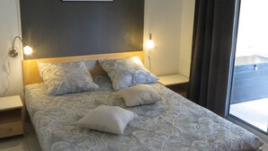 A bedroom with a large bed, two bedside tables, a wall-mounted light, and a window with curtains.