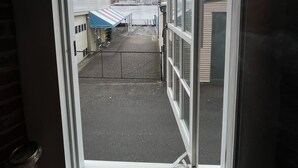 Uitzicht door een raam op een gebouw met een verhard gebied, een blauw gestreept zonnescherm en een boot afgemeerd op de achtergrond.
