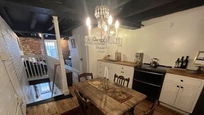 Een eethoek met een houten tafel, stoelen, een kroonluchter en uitzicht op een bakstenen muur en balkon.
