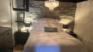 Een slaapkamer met een groot bed, witte beddengoed, een kroonluchter en een stenen muur.