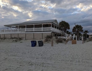 A beach house with a balcony, a wooden fence, and a sandy beach.