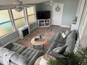 A living room with a grey sofa, a fireplace, a TV, and a bookshelf.