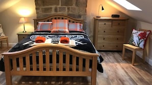 Une chambre confortable avec un plafond en pente, un mur en pierre, un lit en bois et une commode.