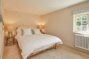 A bedroom with a bed, two bedside lamps, a radiator, and a window with a view of greenery.