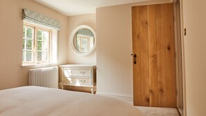 A bedroom with a bed, a dresser, a wooden wardrobe, a window with curtains, and a round mirror.