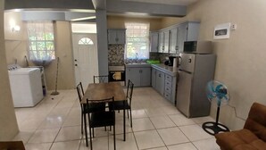 A compact kitchen with a dining area, a washing machine, and a fan.