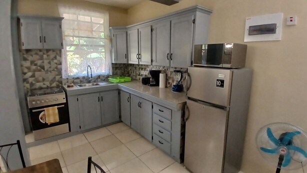 A compact kitchen with grey cabinets, a stove, a sink, a microwave, and a refrigerator.