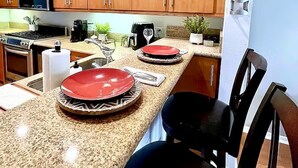 Een moderne keuken met houten kastjes, granieten aanrecht, een inbouwmagnetron, en een eethoek met een zwarte stoel en een rood bord.