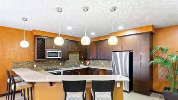 A modern kitchen with a central island, dark wooden cabinets, stainless steel appliances, and pendant lighting.