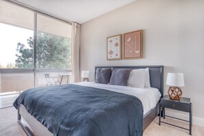 Relax in this serene bedroom with a large bed, nightstand, and a chair near a window offering a view of the surrounding trees.