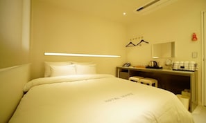 A hotel room with a bed, a desk, a chair, a mirror, and a hanging coat rack.