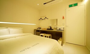 A hotel room with a bed, a desk with a telephone, a mirror, and a small stool.