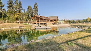 Un chalet au revêtement extérieur en bois, avec un étang devant et une forêt en arrière-plan.
