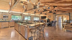 Une cuisine spacieuse dotée d’un grand îlot central, de poutres en bois et d’une cheminée.