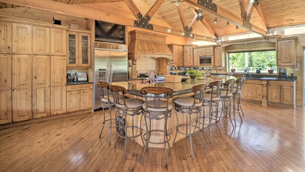 Une cuisine spacieuse avec des meubles en bois, un grand îlot central doté de tabourets de bar et un plafond en bois à voûte.