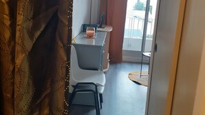 A room with a desk, chair, and a small table with a glass of drink. There is a window with curtains and a view of the outside. - Pleasant T1 hyper center Valras plage (Valras-Plage)