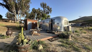 Een vintage caravan met een kleine aanbouw, een houten terras en een cactustuin.