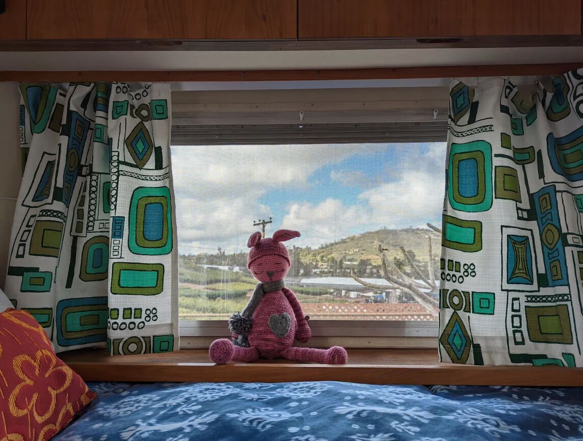 A window with patterned curtains, a teddy bear, and a view of a landscape.